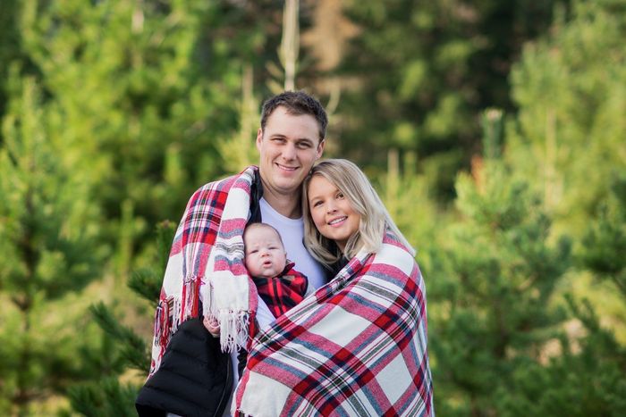 a man and woman are holding a baby wrapped in a plaid blanket .