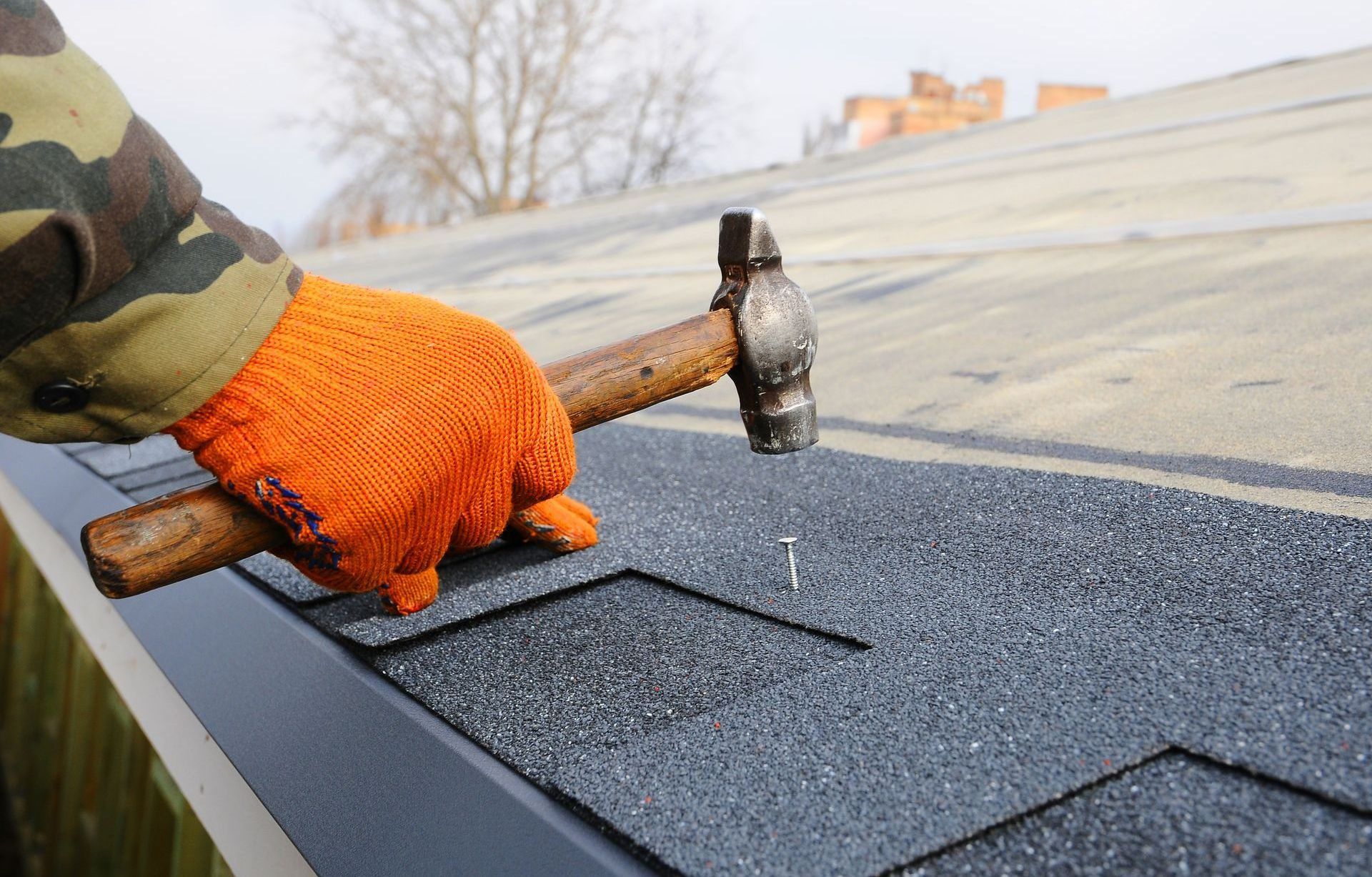 A person is hammering a nail into a roof with a hammer from Washington Roofing Services near Arlington WA